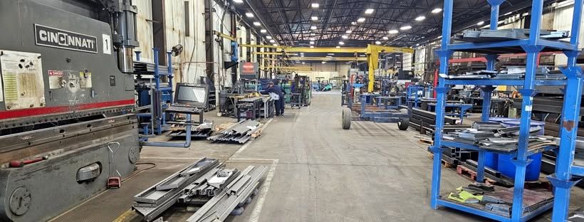 Wisco Metal Solutions shop floor, with a Cincinnati press brake, racks of formed steel parts, and yellow overhead cranes