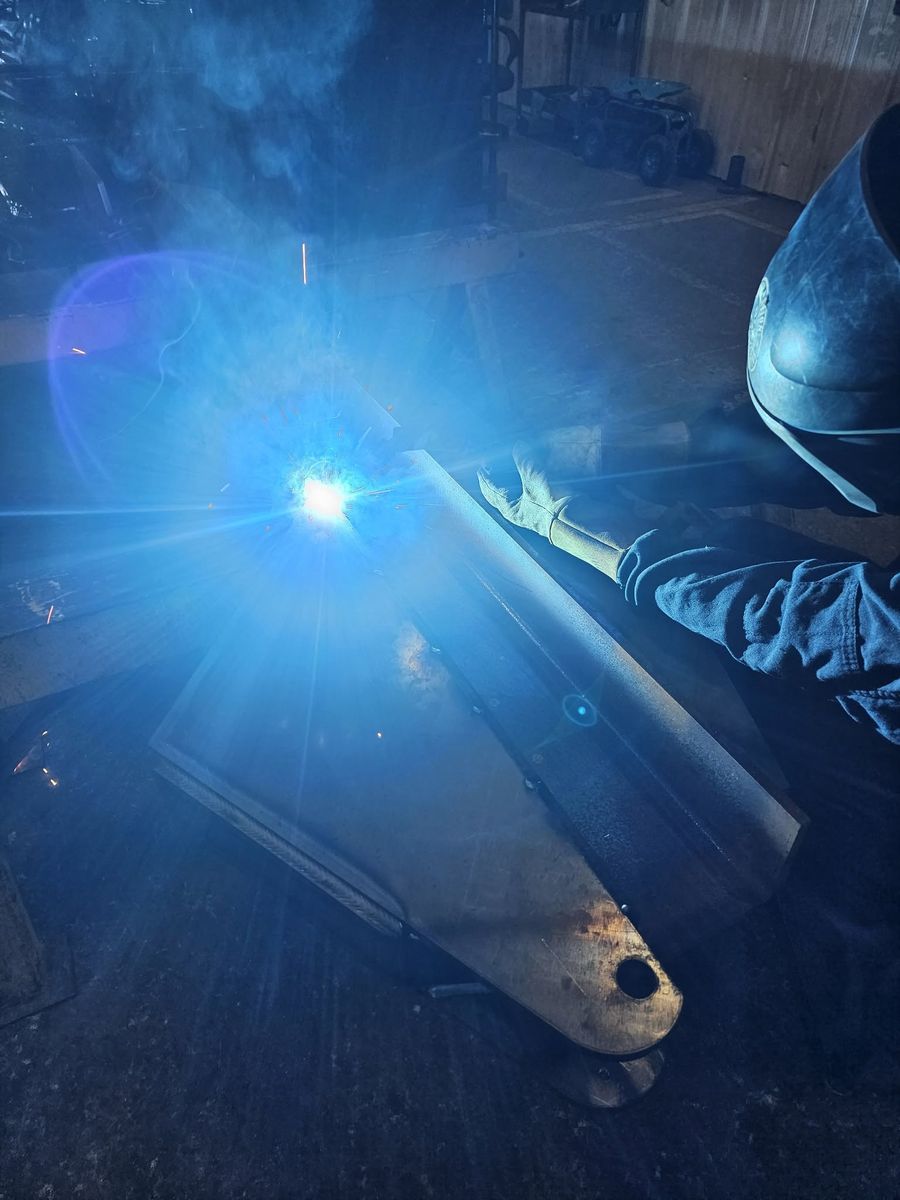 Welder in a helmet and gloves welding a steel plate assembly, with a bright arc and sparks